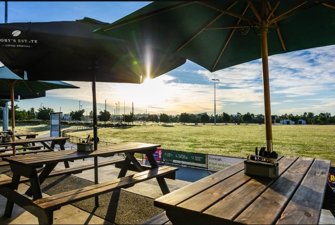 Timber tables under green umbrellas looking out over the Greenbank fields